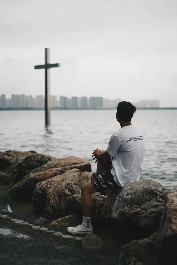 A man sits and looks at a cross that represents Jesus Christ's crucifixion.
